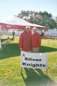 Two people standing behind a 'Silver Knights' sign.
